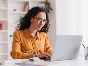 Woman sitting at a desk and typing on a laptop.