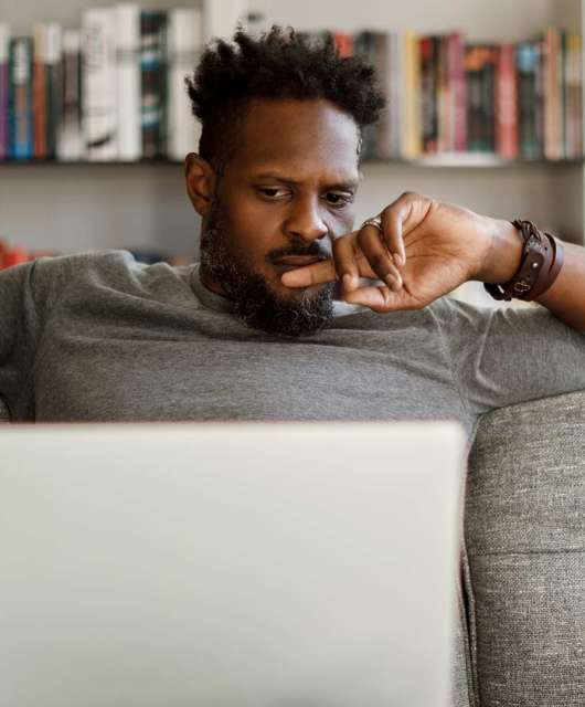 Photo of a man sitting on a couch and looking at a laptop