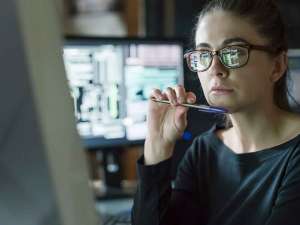 Woman holding pen under her chin looking at a desktop computer.