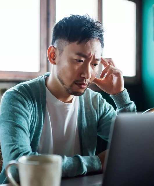 A man sits on his desk looking into his laptop screen and appears stressed.